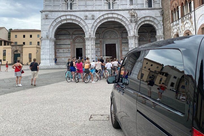 Een groep mensen met fietsen voor een historisch gebouw met bogen. 2