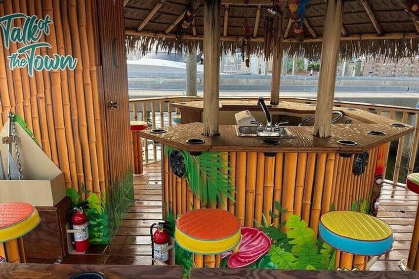 A tiki bar with a thatched roof, bamboo walls, and colorful stools. 4