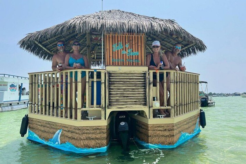 A thatched-roof boat with a wooden deck, passengers, and calm water. 2