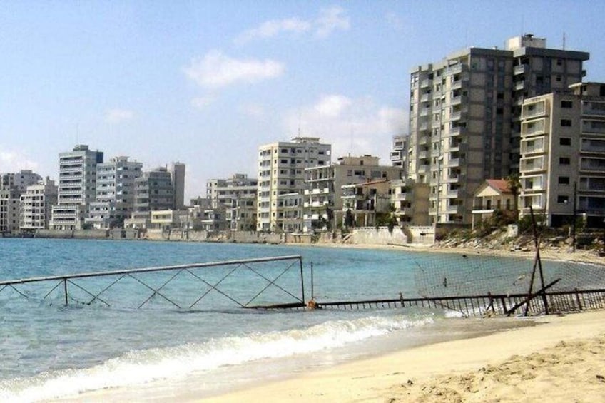 Een strand met een metalen hek en gebouwen op de achtergrond. 1