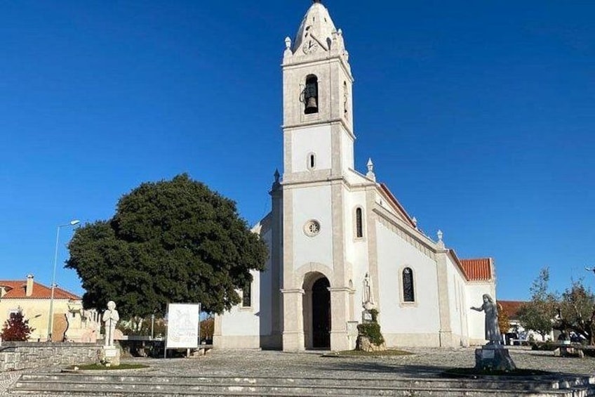 Una iglesia con un campanario, un árbol grande en primer plano y un cielo azul despejado. 3