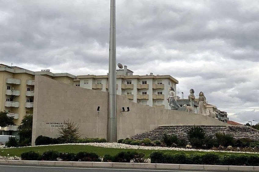 Un edificio con una estatua, un poste alto y un área ajardinada con plantas. 5