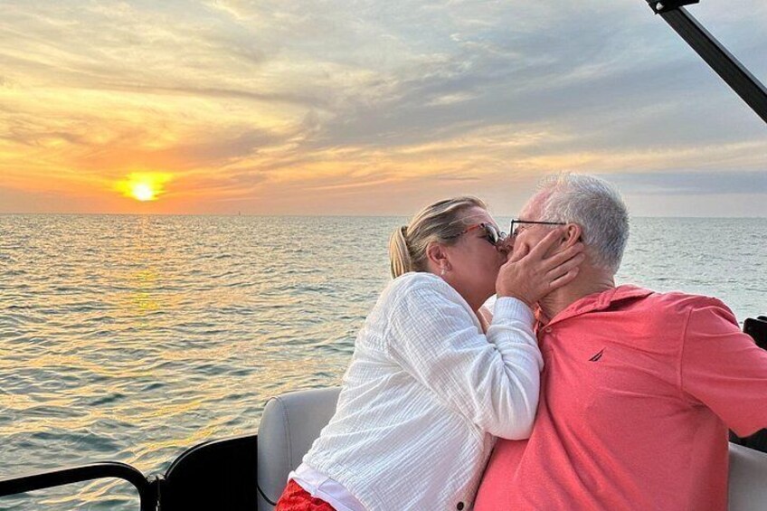 Una pareja abrazándose en un barco con un atardecer de fondo. 4