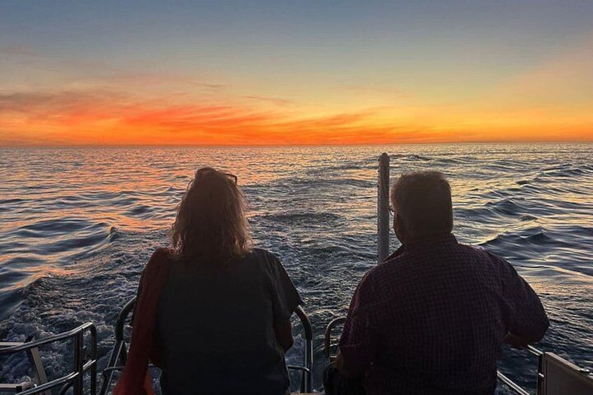 Dos personas en un bote al atardecer, con mar tranquilo y cielo colorido. 2