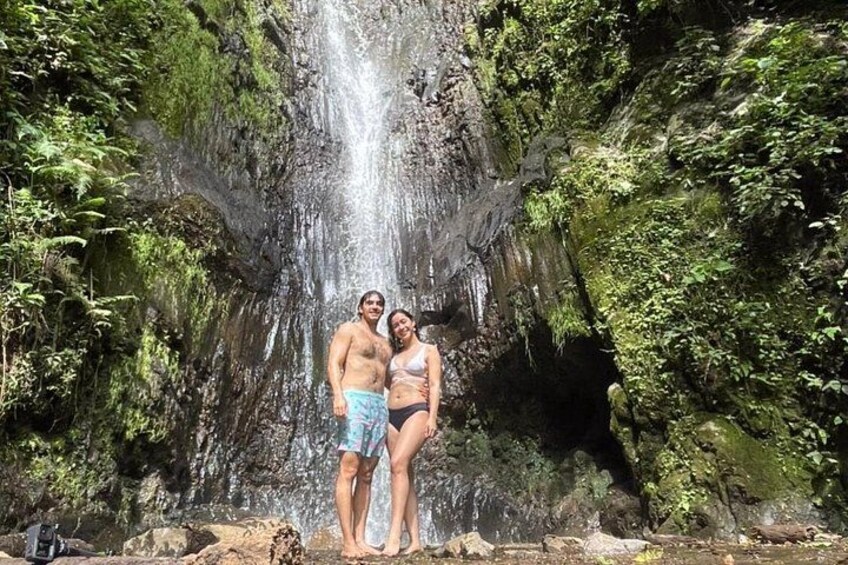 Een waterval omringd door weelderige begroeiing, met twee personen ervoor. 5
