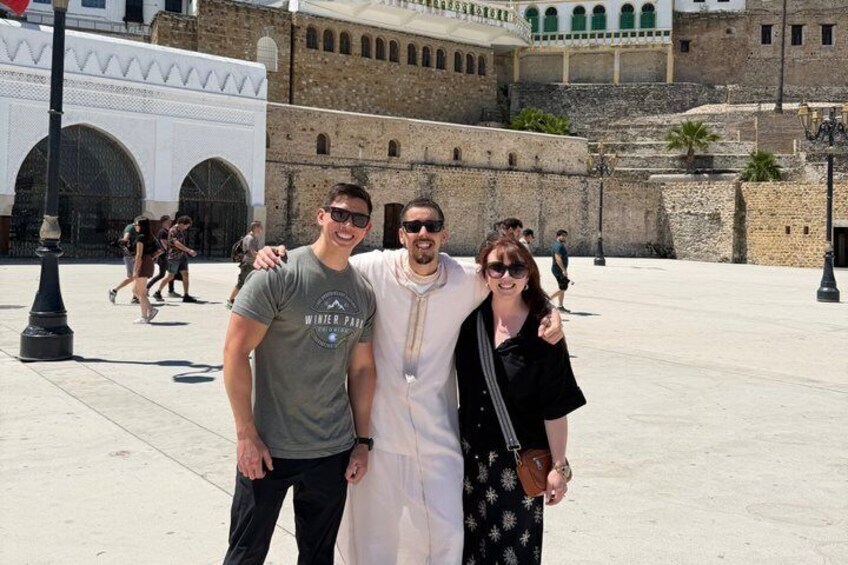 A group of people posing in front of a historic building with arches and a fortified wall. 4