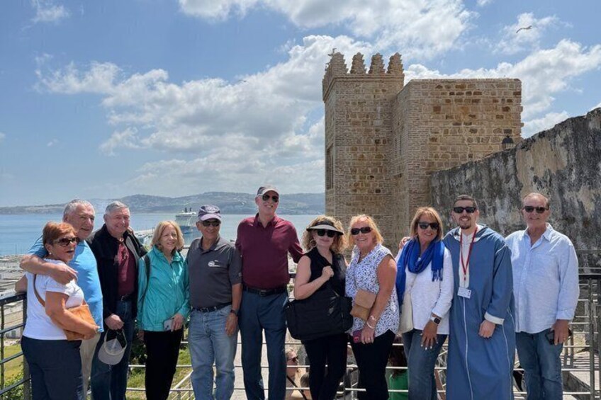 A group of people standing in front of a historic stone tower by the sea. 3