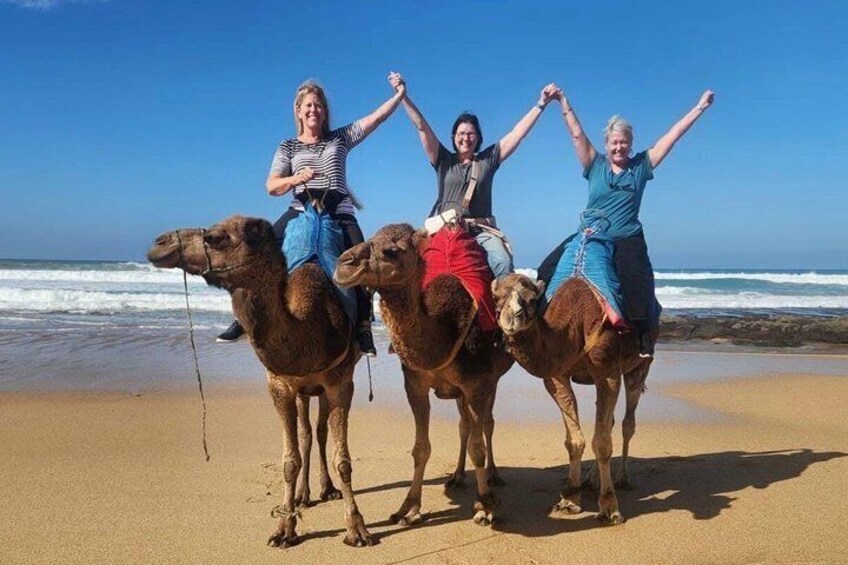 Three people riding camels on a beach with the ocean in the background. 2