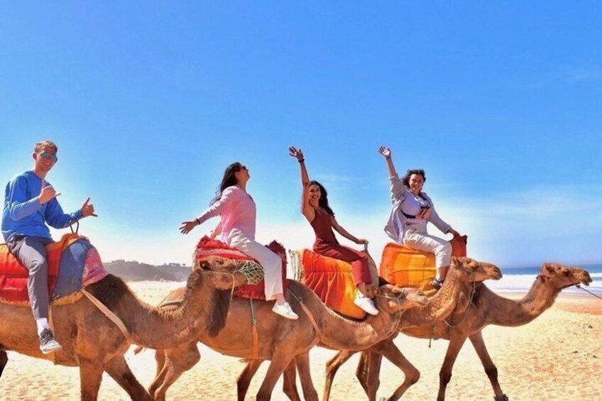 Four people riding camels on a beach. 1