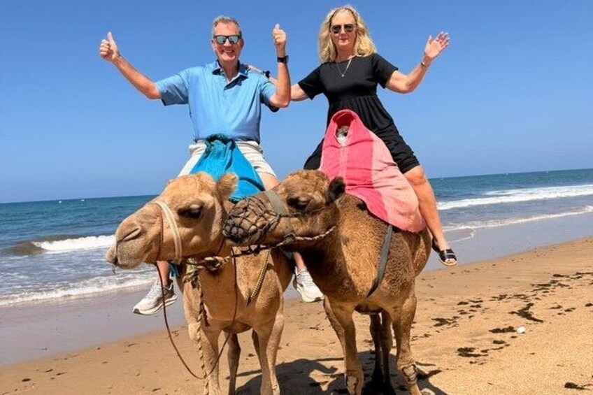 Two people riding camels on a beach with the ocean in the background. 5