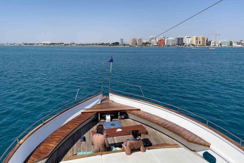 A boat with a wooden deck, two people sitting, and a city skyline in the background. 3