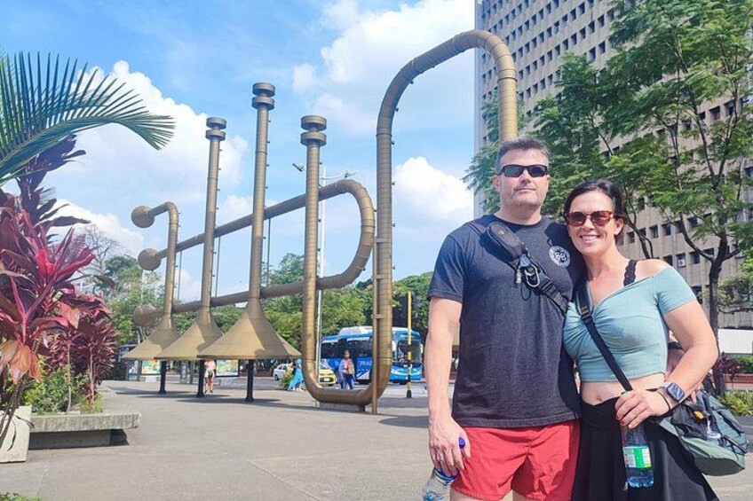 Una pareja posa frente a una gran escultura abstracta con tuberías y embudos. 4