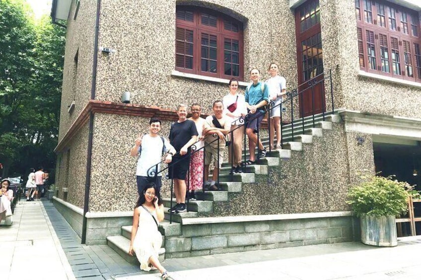 A group of people on a stone staircase outside a building with red-framed windows. 1