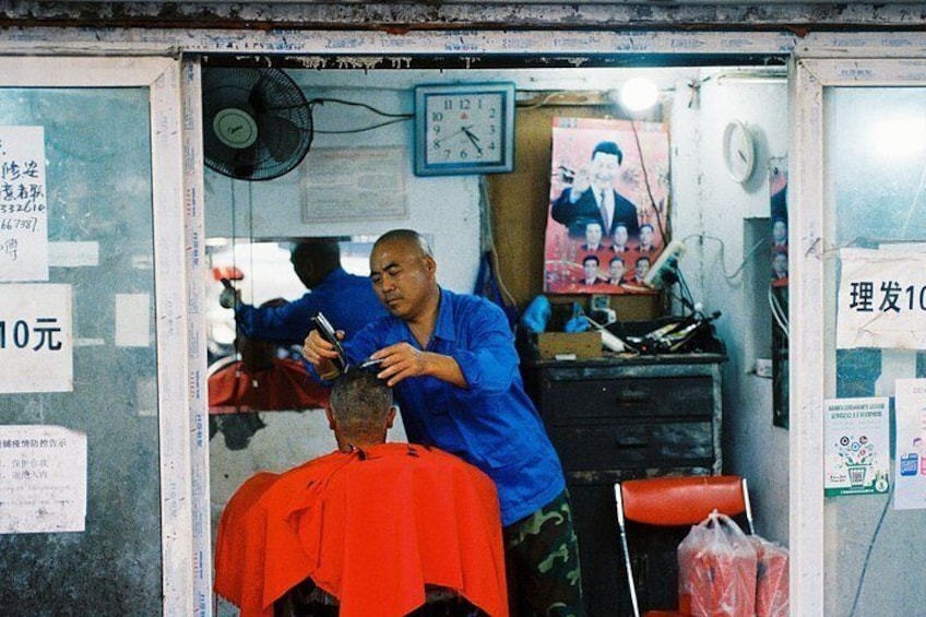 A barber shop interior with a barber cutting a customer's hair. 2