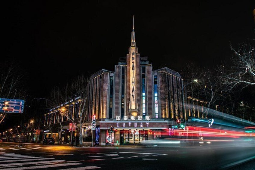 A brightly lit building with a tall spire, surrounded by illuminated signs and a busy street with light trails. 4