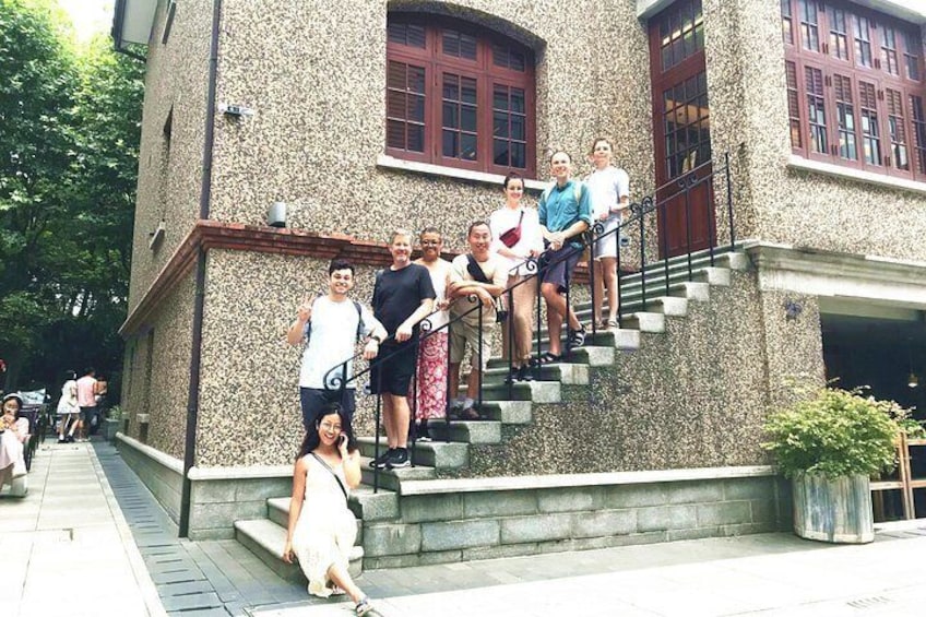 A group of people on a stone staircase in front of a building with red-framed windows. 1