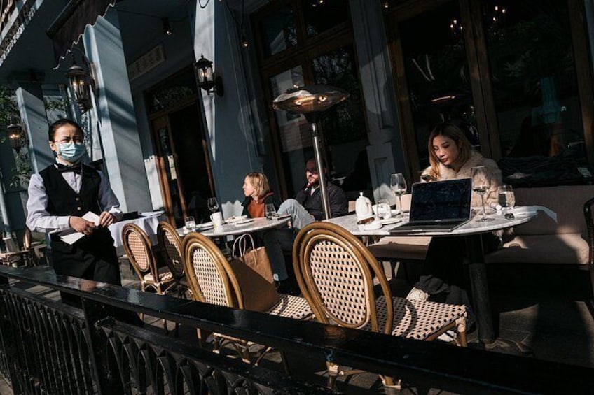 An outdoor cafe with tables and chairs, a waiter, and patrons. 3