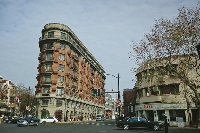 A curved multi-story building with a brick facade, a street with cars, and a tree with sparse leaves. 5
