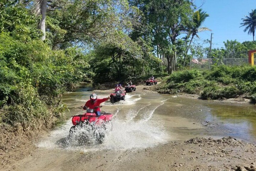 Des personnes conduisent des quads rouges sur un chemin boueux, au bord d’une rivière. 1