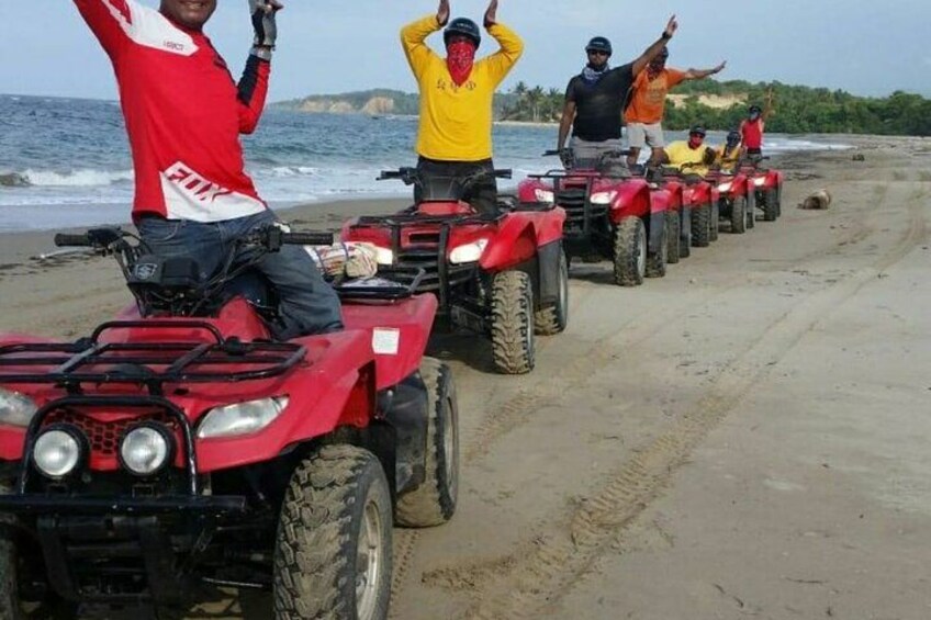 Un groupe de personnes à bord de quadros rouges s’est aligné sur une plage de sable, avec l’océan en toile de fond. 4