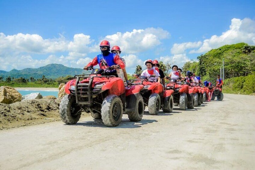 Un groupe de personnes circule à bord de quad rouges sur un chemin de terre, avec un paysage montagneux en arrière-plan. 5
