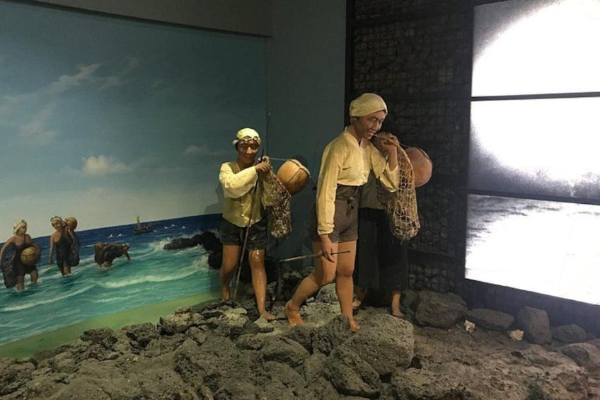 Una exhibición de museo con escena de playa, que incluye figuras de personas y animales, y una pantalla grande mostrando una vista de playa. 3