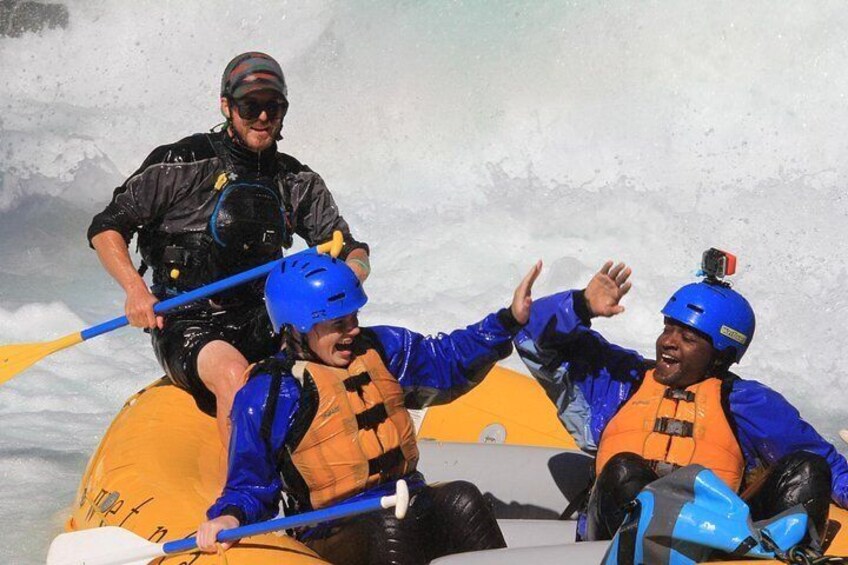 Two people in a yellow raft wearing blue helmets and orange life jackets, paddling through a river. 2