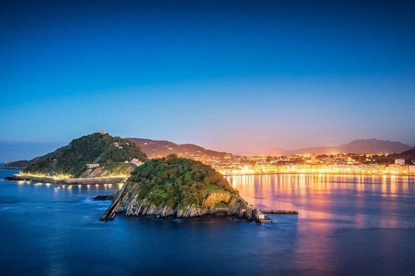 A coastal landscape with a prominent island, calm waters, and a distant cityscape at twilight. 2