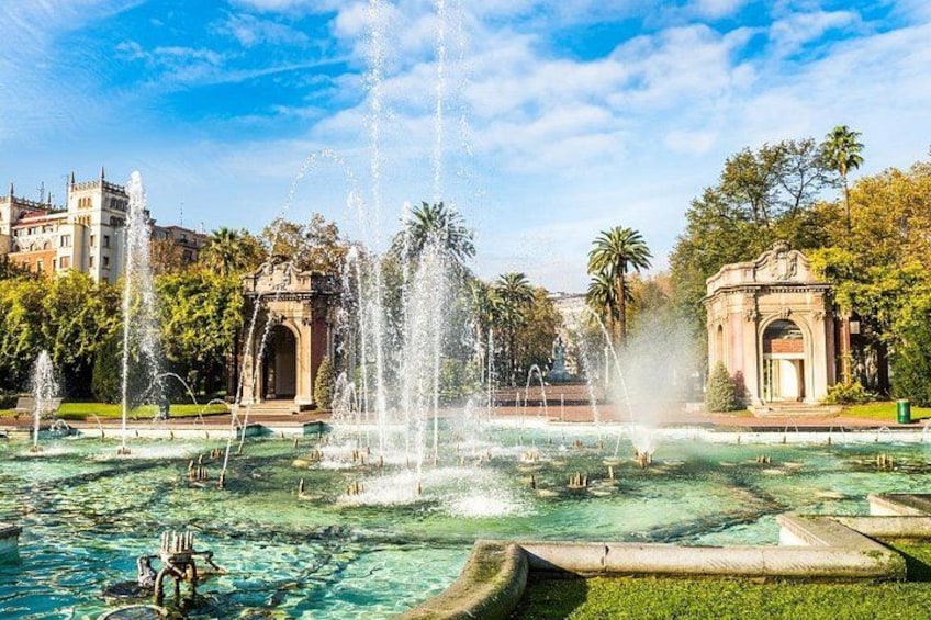 A fountain with water jets, surrounded by greenery and historic buildings. 4