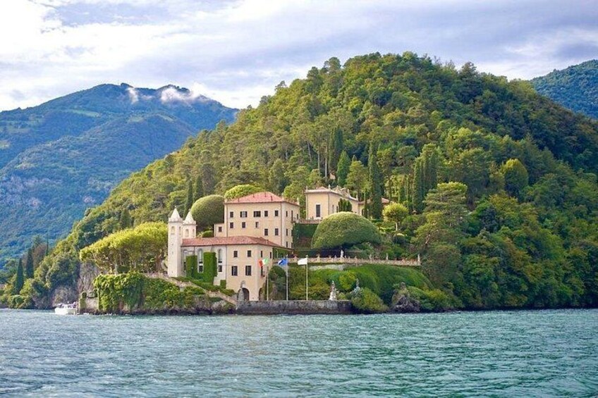 A lakeside villa with a tower, surrounded by lush greenery and mountains. 4
