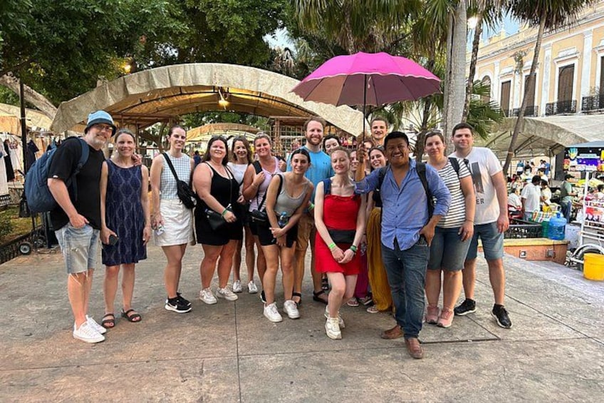 Een groep mensen die samen op de foto gaat op een openbaar plein, met een markt op de achtergrond. 2