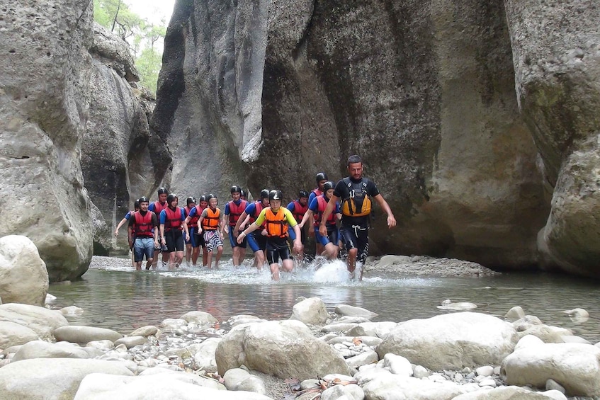 A group of people crossing a river in a rocky canyon. 1