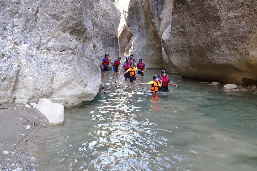 A group of people wading through a narrow canyon with rocky walls and a clear stream. 5