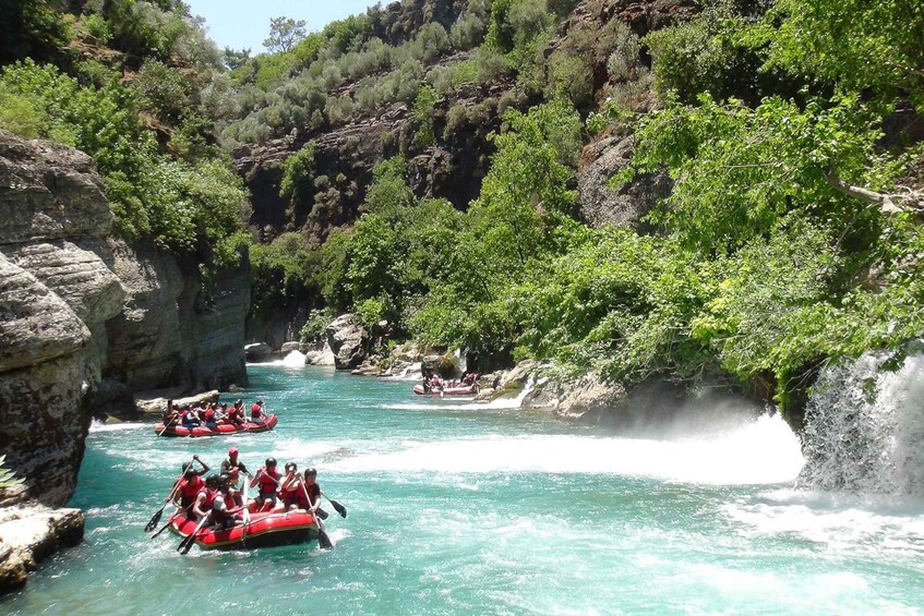 A group of people rafting down a turquoise river surrounded by rocky cliffs and lush greenery. 2