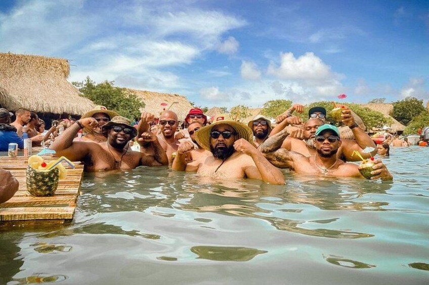 A group of people in a swimming pool with a thatched-roof structure in the background. 3