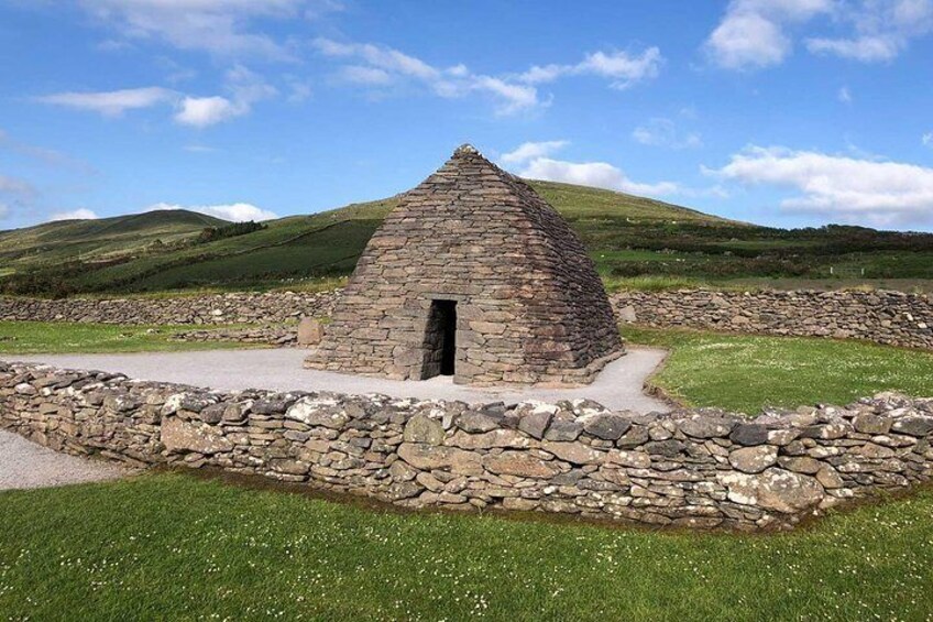 A stone structure with a triangular roof, surrounded by a stone wall and grassy area. 3