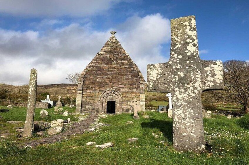 A stone church with a pointed roof, surrounded by grassy fields and several large stone crosses. 2