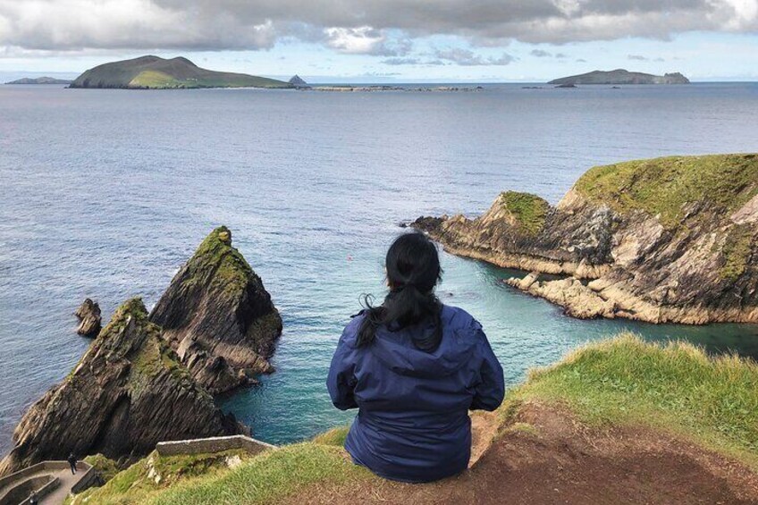A person sitting on a cliff overlooking a coastal landscape with rocky outcrops and calm sea. 5