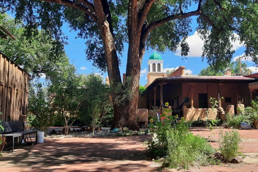 A rustic outdoor setting with a large tree, a wooden building, and a distant church with a green dome. 4