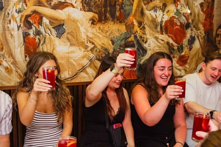 A group of people holding red drinks, seated in a room with a large floral mural on the wall. 2