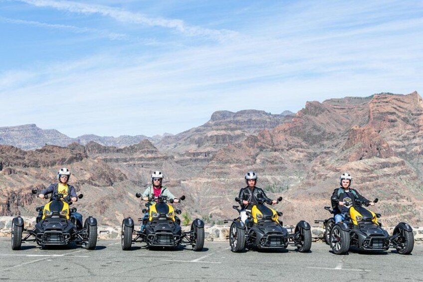 Quattro persone su quad in un parcheggio, con un paesaggio montuoso sullo sfondo. 4
