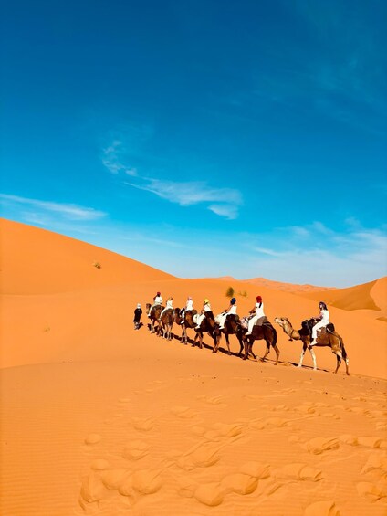 A group of people riding camels across a desert landscape with sand dunes under a clear blue sky. 1