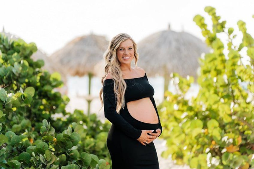 A pregnant woman in a black dress standing in a lush green garden with a mountain in the background. 2