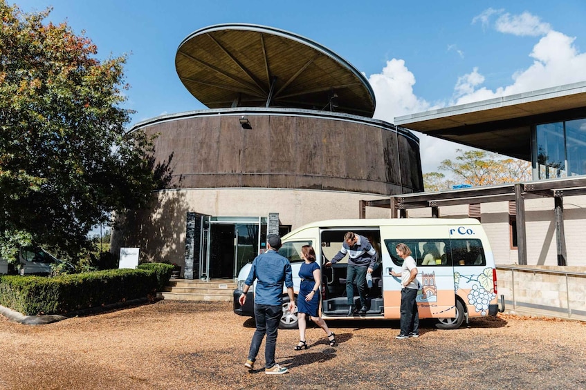 Een groep mensen stapt een toeristenbus op voor een modern gebouw met een groot, rond dak. 1