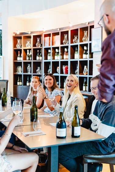 A group of people sitting at a table with wine bottles and glasses. 1