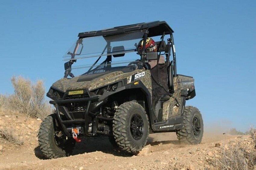 A camouflage off-road vehicle with a driver, in a desert environment. 2