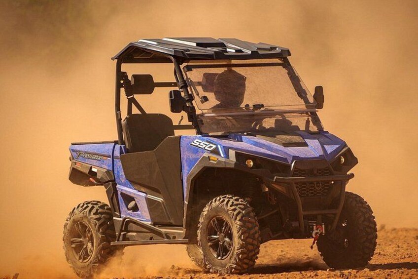 A blue off-road vehicle with large tires and a roof, driving through a dusty area. 3