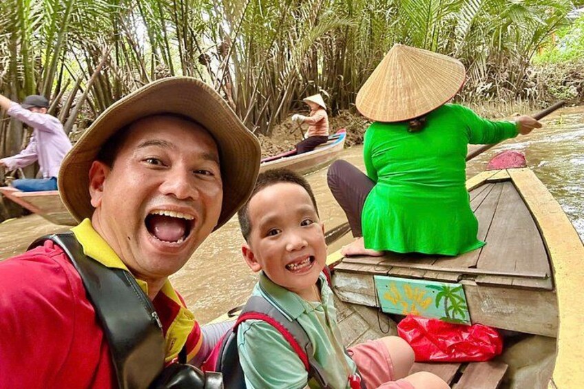 A person in a boat, another in a green dress, and a third in a hat, with a river and palm trees in the background. 1