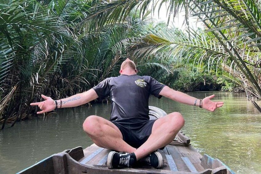 A person sitting cross-legged on a boat in a waterway surrounded by dense tropical vegetation. 2