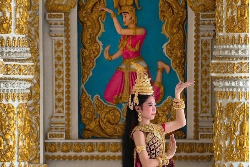 A person in traditional attire performing a dance in front of a mural with intricate gold detailing. 4